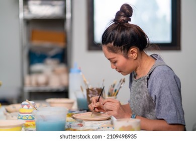 Asian Woman Learning Color Painting Her Self-made Pottery Plate At Home. Confidence Female Relax And Enjoy Handicraft Activity Lifestyle Hobbies Ceramic Sculpture Painting Workshop At Pottery Studio