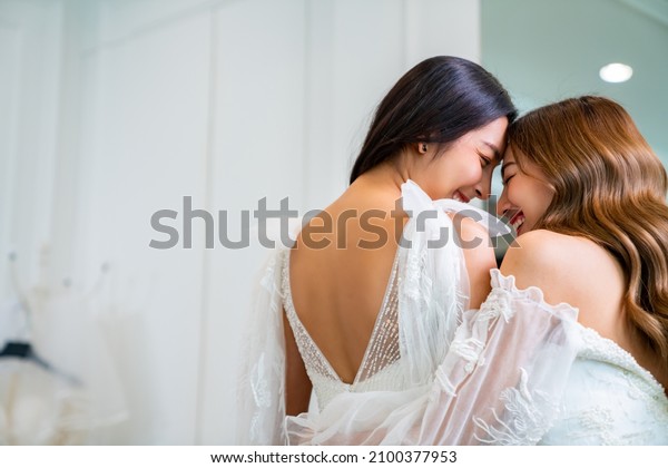 Asian woman lesbian couple choosing and trying\
on wedding dress for marriage ceremony in bridal shop together.\
Diversity sexual equality, lgbtq pride, marriage equality and\
Same-sex marriage\
concept.