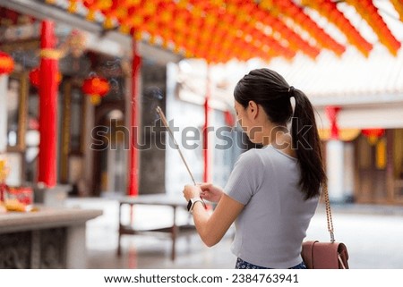 Asian woman lighting incense sticks to pray in Chinese temple