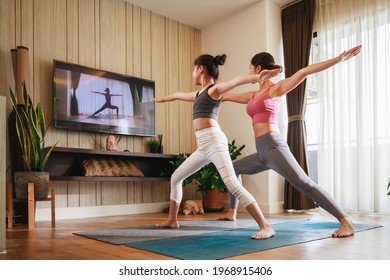 Asian woman and Little girl practicing yoga from yoga online course via smart TV at home. Healthy lifestyle - technology at home. New normal lifestyle. Home Online Stretching Yoga Fitness Exercise.