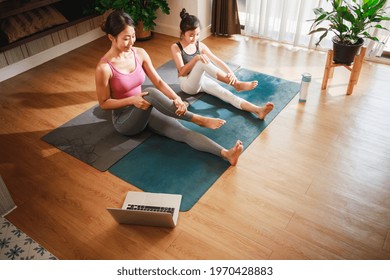 Asian woman and Little girl practicing yoga from yoga online course via laptop at home. Healthy lifestyle - technology at home. New normal lifestyle. Home Online Stretching Yoga Fitness Exercise.