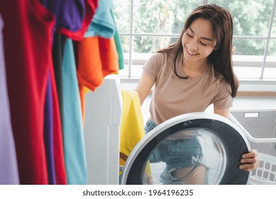 Asian Woman Loading Dirty Clothes In Washing Machine In Laundry Room.