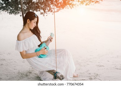 Asian Woman Lonely Playing Ukulele Sitting On Swing At Beach With Acoustic Classic Song Wearing White Dress Solitude Alone,sad Love On Summer Season 