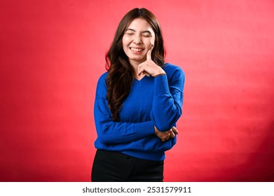 Asian woman with long hair, wearing a blue sweater, poses with a playful and exaggerated thoughtful expression. touches her forehead with her finger while standing a red background. - Powered by Shutterstock