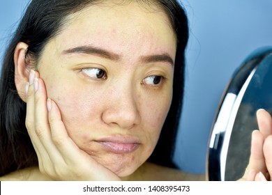 Asian woman looking at herself in the mirror, Female feeling annoy about her reflection appearance show the aging facial skin signs, wrinkles, dark spot, pimple, acne scar, large pores, dull skin. - Shutterstock ID 1408395473