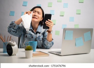 Asian Woman Looking At Smart Phone Reading News Crying And Using Tissue Paper At Home Office. WFH. Work From Home. Prevention Coronavirus COVID-19 Concept.