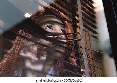 Asian woman looking through window blinds spying on neighbours - Young lonely millennial woman peeping through glass observing gossip and action outdoors - introvert, privacy and intrusive concepts - Powered by Shutterstock