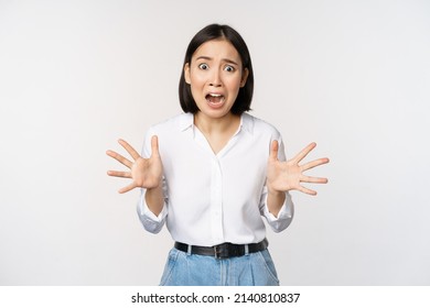 Asian woman looks at camera and screams in panic. Young korean girl looking anxious, panicking, shaking hands and shouting, standing over white background