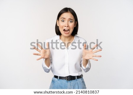 Asian woman looks at camera and screams in panic. Young korean girl looking anxious, panicking, shaking hands and shouting, standing over white background