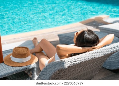 Asian woman lying down on sunbed near swimming pool. Young traveler female sunbathing at hotel during her summer vacation trip. Summer and holiday concept. Copy space, Closeup