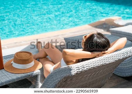 Asian woman lying down on sunbed near swimming pool. Young traveler female sunbathing at hotel during her summer vacation trip. Summer and holiday concept. Copy space, Closeup