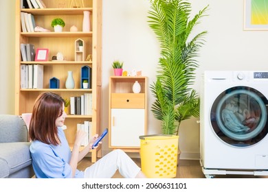 Asian Woman Lying On Floor Do The Laundry In Smart Washing Machine And Use Smartphone Operate It At Home