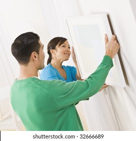 Asian Woman And Male Hanging Art On Wall. Square Composition.