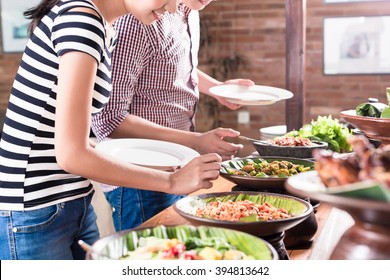 Asian Woman And Man Choosing Food At Indonesian Buffet In Restaurant