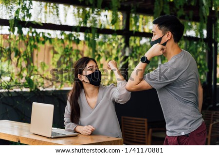 Asian woman and man friends wearing face mask outdoors. Friends greeting and shaking with elbows as new normal. Corona Virus - Covid 19 elbow bumps greeting style to prevent contact and virus spread.
