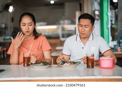 Asian woman and man sitting with a spicy expression while eating pecel in a traditional food stall - Shutterstock ID 2330479561