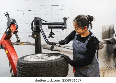 Asian woman mechanic operating a tire changing machine while repairing a wheel in a busy car service garage, showcasing her skills and expertise - Powered by Shutterstock