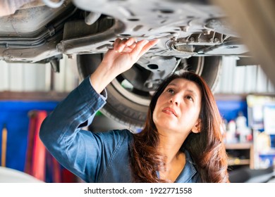 Asian Woman Mechanic Working Under Vehicle In A Car Service. Empowering Woman Using Wrench Underneath The Car. 