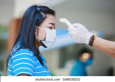 Asiatische Frau in medizinischer Schutzmaske, die sich vor der Arbeit im Büro einer Temperaturkontrolle unterzieht.Quarantäne oder Vorsorgeerkrankung. Ausbruch der Covid-19-Ausbreitung 