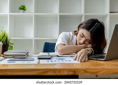 Asian woman napping at her desk, Businesswoman snoozing at her desk after working for a long time causing fatigue and sleepiness, she is resting. Hard work concept.