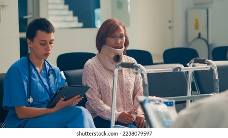 Asian woman with neck brace collar doing consultation with nurse, writing medical report on digital tablet. Wearing cervical foam after fracture injury, talking to healthcare specialist. - Powered by Shutterstock