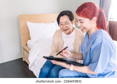 Asian Woman Nurse Wearing Scrubs Report The Health Status Of Senior Asian Woman With Digital Tablet In The Bedroom. Caregiver Visit At Home. Home Health Care And Nursing Home Concept.