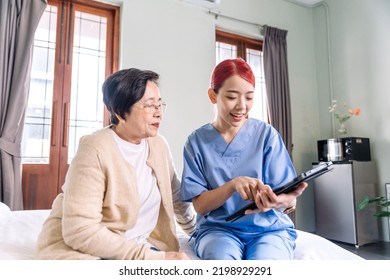 Asian Woman Nurse Wearing Scrubs Report The Health Status Of Senior Asian Woman With Digital Tablet In The Bedroom. Caregiver Visit At Home. Home Health Care And Nursing Home Concept.