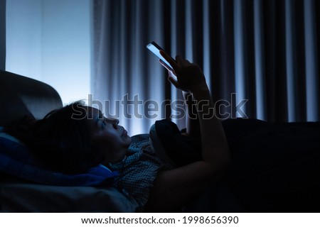 Asian woman on bed late at night and using mobile smartphone before sleep in dark bedroom