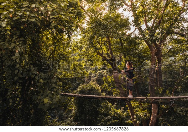 Asian Woman on the canopy walk\
(tree top walk), new activity for travel in the forest by walking\
across the long wooden bridge in Chiang rai, north of\
thailand