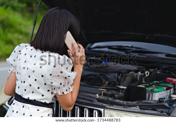 Asian woman on car. Asian woman\
looking at the car broken. car is broken, waiting for\
Mechanic.