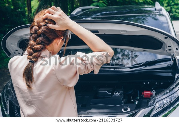 Asian woman opened car hood for looking the problem\
of car breakdown while waiting for assistance on the road side. Car\
breakdown it will happen to you at least once in your driving\
life.