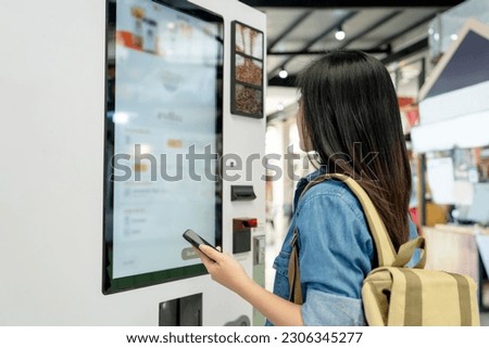 Asian woman ordering drink from touch screen electronic machine in shopping mall, electronic menu.