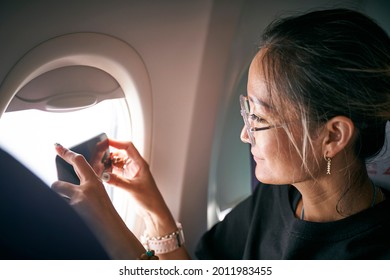 Asian Woman Passenger Taking A Picture Using Mobile Phone In Airplane Cabin