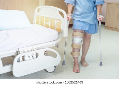 Asian Woman Patient With Knee Brace With Walking Stick In Hospital Ward After Ligament Surgery.
