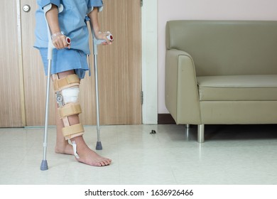 Asian Woman Patient With Knee Brace With Walking Stick And Knee Braces Support In Hospital Ward After Ligament Surgery.
