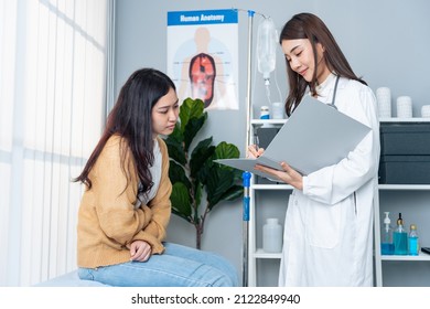 Asian Woman Patient Visit And Consult Health Problem With Young Doctor. Sick Girl Feel Hurt And Painful Suffering From Stomach Ache Then Explain To Attractive Therapist Practitioner In Office Hospital