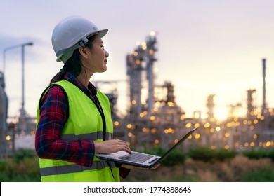 Asian woman petrochemical engineer working at night with laptop Inside oil and gas refinery plant industry factory at night for inspector safety quality control.