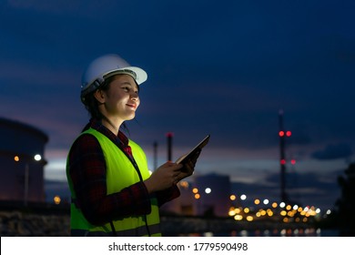 Asian woman petrochemical engineer working at night with digital tablet Inside oil and gas refinery plant industry factory at night for inspector safety quality control.