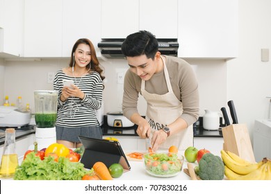 Asian Woman With Phone While A Man Prepares A Meal