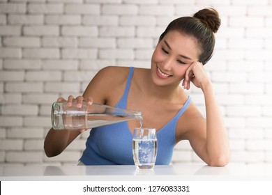 Asian Woman Pouring Water From Bottle Into Glass In The Room