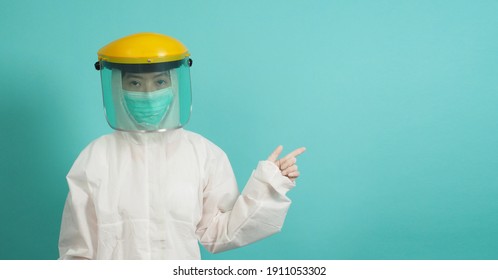 Asian Woman In PPE Suit , Face Shiled,medical Gloves And Wear Face Mask  Is Pointing Finger On Green, Tiffany Blue Background.