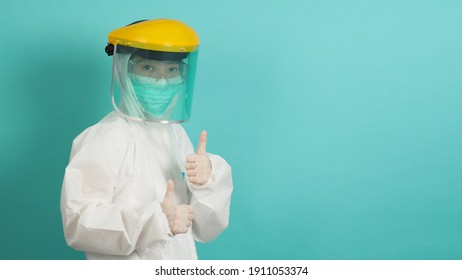 Asian Woman In PPE Suit , Face Shiled,medical Gloves And Wear Face Mask  Do Thumb Up Or Like Hand Sign On Green, Tiffany Blue Background.