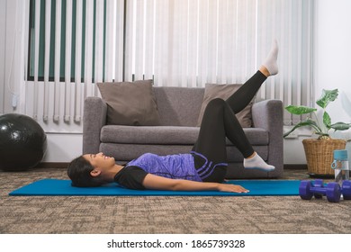 Asian woman practicing yoga at home while lying on a mat and stretching her legs. - Shutterstock ID 1865739328