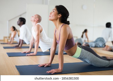 Asian Woman Practicing Yoga Positions During Group Training At Gym, Performing Back Bending Asana Urdhva Mukha Shvanasana (Upward Facing Dog Pose)