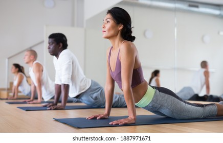 Asian Woman Practicing Yoga Positions During Group Training At Gym, Performing Back Bending Asana Urdhva Mukha Shvanasana (Upward Facing Dog Pose)