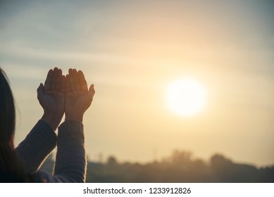 Asian woman praying and hopeful for peace the world and free from coronavirus, Christian women raise hands in hands together with sunrise background, believes, and faith in Christian religion. 