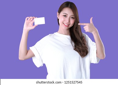 Asian woman present a blank credit card, white t-shirt clothing, purple background