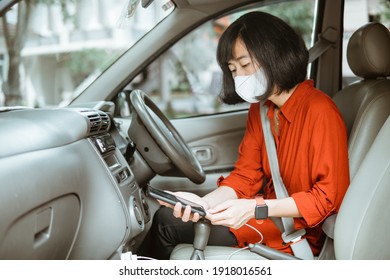 asian Woman in protective mask driving a car on road. charge her phone