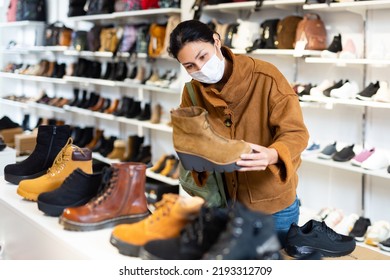 Asian Woman In A Protective Mask, Who Came To A Shoe Store For Shopping During The Pandemic, Chooses Autumn Halfboots ..with High Soles