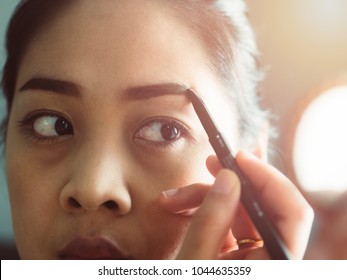 Asian Woman Is Putting Make Up On Her Eyebrows With The Eyebrows Pencil.